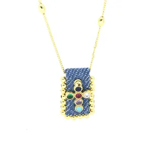 Dettaglio del ciondolo a croce vintage bohémien con zirconi colorati su denim