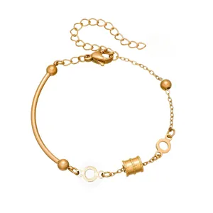 Close-up detail of a gold-plated stainless steel bracelet featuring a geometric cylinder charm