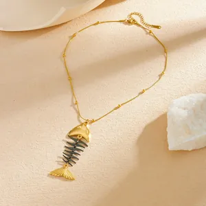 Detailed view of a gold-plated titanium steel fishbone pendant necklace on textured surface.