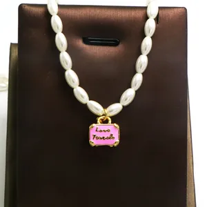 Detail view of a pearl necklace with a pink suitcase pendant engraved with Love Travels.