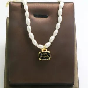 Detail shot of pearl necklace featuring a black suitcase pendant with Love Travels