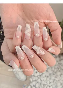 Primo piano di unghie eleganti decorate con perle bianche e strass trasparenti brillanti.