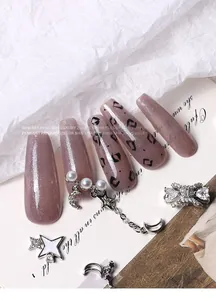 Detailed view of silver zircon butterfly and pearl moon pendant charms on mauve glitter nails