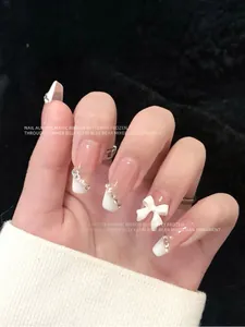 Gedetailleerd overzicht van elegante witte 3D-strik en fonkelende strass-nageldecoraties.