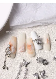 Close-up of pearl and butterfly nail charms with dangling chains on beige nail art.