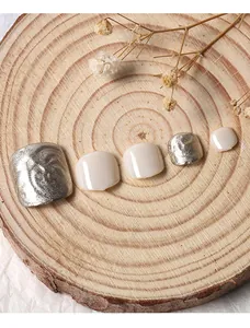 Gros plan d'ongles d'orteils argentés et crème présentés sur un bloc de bois naturel
