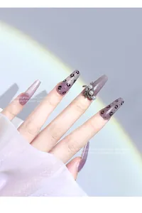 Close-up of purple glitter press-on nails featuring a butterfly charm and pearls