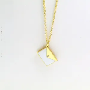 Detailed macro shot of a gold-plated envelope necklace with white enamel and a tiny crystal.