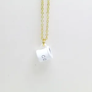 Detailed macro view of white enamel coffee cup pendant on a delicate gold chain necklace