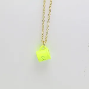 Macro detail shot showing neon yellow drip oil coffee cup pendant on thin gold link chain