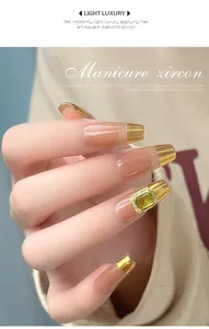 Close-up of a square yellow zircon nail art accessory on a gold tipped manicure.