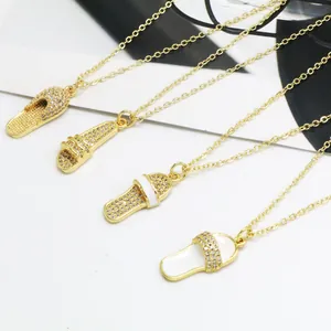 Detail view of four gold slipper-shaped necklaces with rhinestones and white enamel