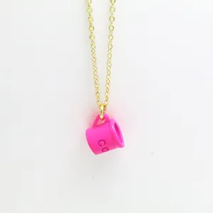 Close-up detail of a bright pink coffee cup pendant on a delicate gold chain necklace.