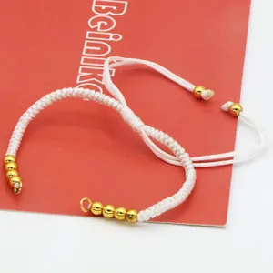 Nahaufnahme eines weiß geflochtenen Armbands mit verstellbarem Schiebeknoten und Goldperlen