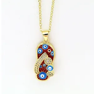 Close-up of a gold flip-flop pendant necklace featuring Evil Eye charms and red enamel