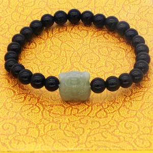 Macro detail of black obsidian beads and green nephrite jade tiger charm on bracelet