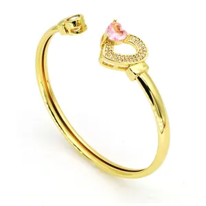 Gros plan sur un jonc doré avec une pierre de cœur rose et des détails en zircon brillant.