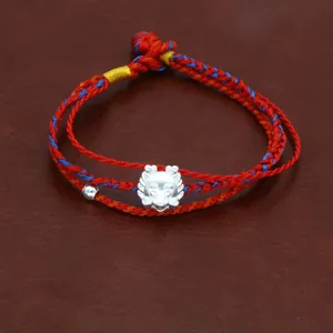 Detail van een gevlochten rode armband met zilveren draak voor het sterrenbeeld 2024