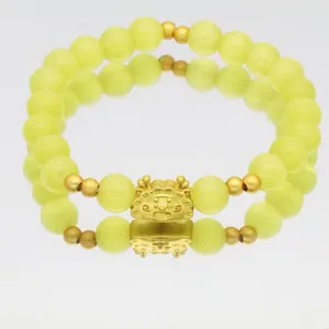 Detailansicht eines gelben Katzenaugen-Perlenarmbands mit süßem goldenen Drachenanhänger