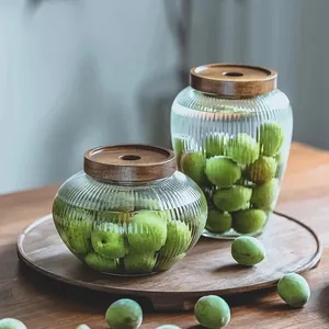 Details of fluted glass storage jars with acacia wood lids filled with green plums.