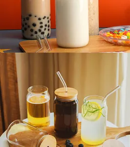 Close-up of clear can-shaped glass cups with bamboo lids and straws in a lifestyle setting