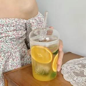 Close-up of a 500ml borosilicate glass cup with a dome lid and glass straw held by a person
