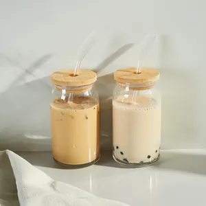 Close-up of 16oz can-shaped glass cups with bamboo lids and straws in a modern setting.