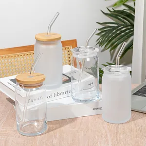 Group of can-shaped glass cups with bamboo lids and glass straws on white books