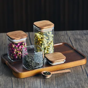 Quadratische Glasvorratsgläser mit Akazienholzdeckeln auf Tablett für Tee und Blumen