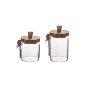 Set of two clear glass storage jars featuring acacia wood lids and small wooden spoons