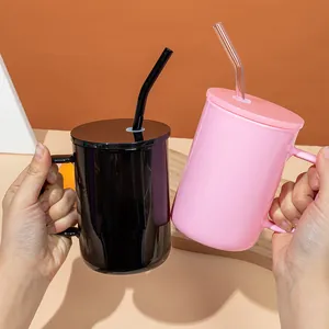 Close-up of hands holding 17oz black and pink glass mugs with matching lids and glass straws.