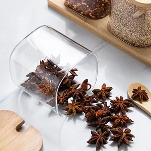 Nahaufnahme von Sternanis, der aus einem klaren Glas-Gewürzstreuer mit Holzlöffel fällt.