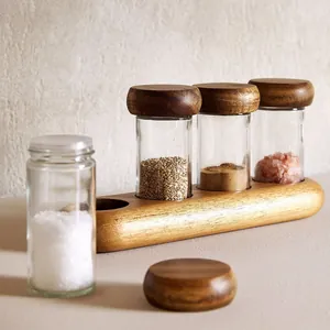 Detailed shot of glass spice jars with acacia wood lids and a minimalist wooden base.