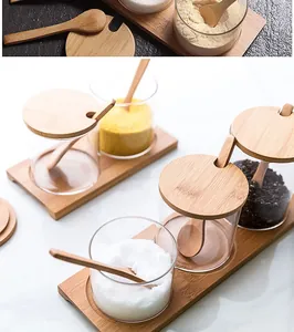 Detailed view of glass seasoning jars with bamboo lids and spoons on a wood tray