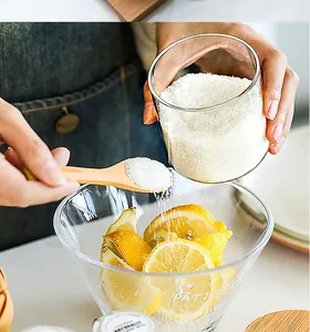 Detail of a transparent glass jar and wooden spoon pouring sugar over fresh lemons.