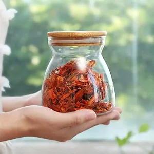 Trapezoidal transparent glass storage jar with bamboo lid held in hands for size reference.