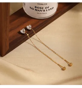 Detailed view of heart CZ long chain earrings on an elegant wooden and fabric background.