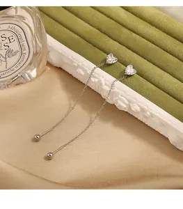 Close-up detail of silver titanium steel long chain earrings with heart-shaped zircon stones