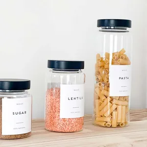 Three glass food storage jars with black lids and minimalist labels on a wooden surface.