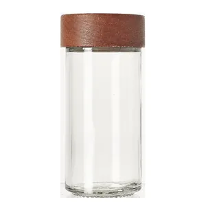 Cylindrical glass spice jar with dark acacia wood lid on plain white background