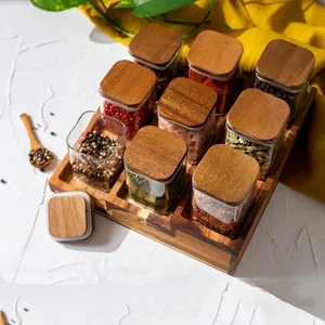 Detail view of square glass spice jars with acacia wood lids on a wooden base.