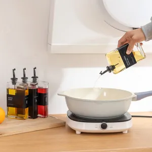 Olijfolie die uit een glazen fles in een koekenpan op het fornuis wordt gegoten