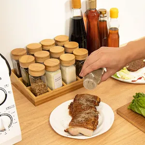 Action shot of square glass spice jar with bamboo lid seasoning cooked meat on a counter