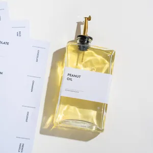 Detail van een vierkante glazen oliefles met een gouden schenktuit en etiket.