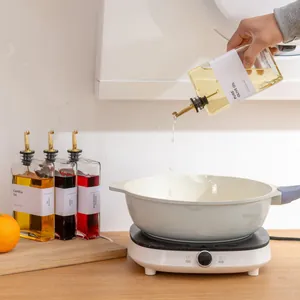 Detail van het gieten van olie uit een vierkante glazen dispenser van 500 ml in een pan.