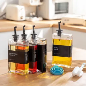 Set vierkante glazen oliedispenserflessen met zwarte labels in een lichte keukenomgeving