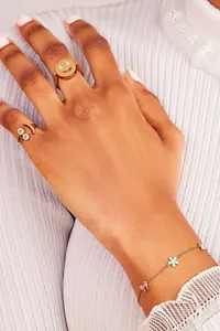 Detailed shot of gold smiley face rings and flower charm bracelet on a person's hand