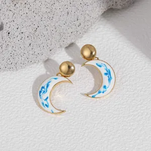 Detailed view of blue and white porcelain pattern moon-shaped earrings with gold posts.