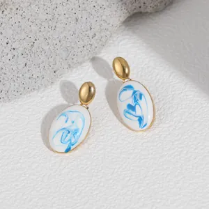 Close-up of blue and white enamel drop earrings with gold-tone accents on textured stone