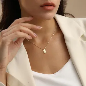 Detail view of 18K gold initial necklace with engraved 'R' pendant on a model.